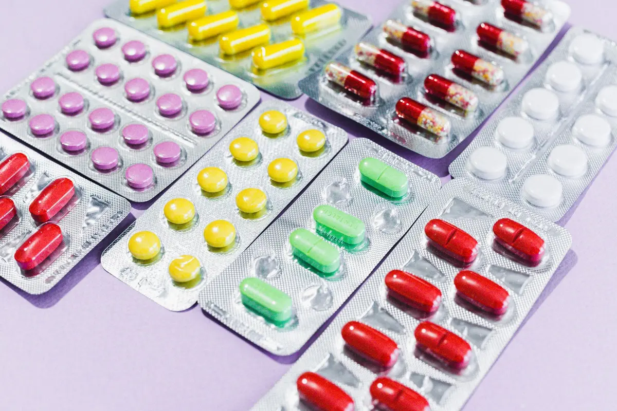 Medicamentos y cajas en estante de farmacia, mano de cliente alcanzando un producto