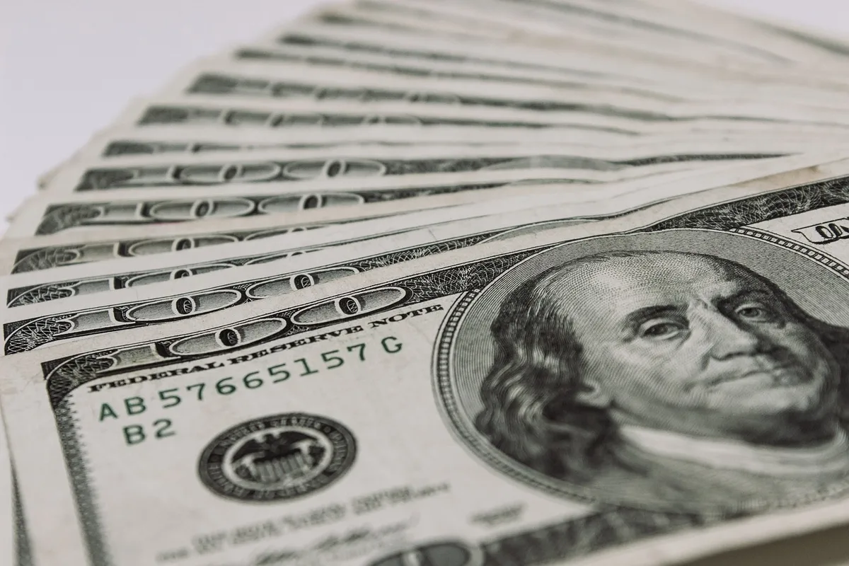 Billetes de peso y dólar sobre escritorio con gráficos financieros de fondo