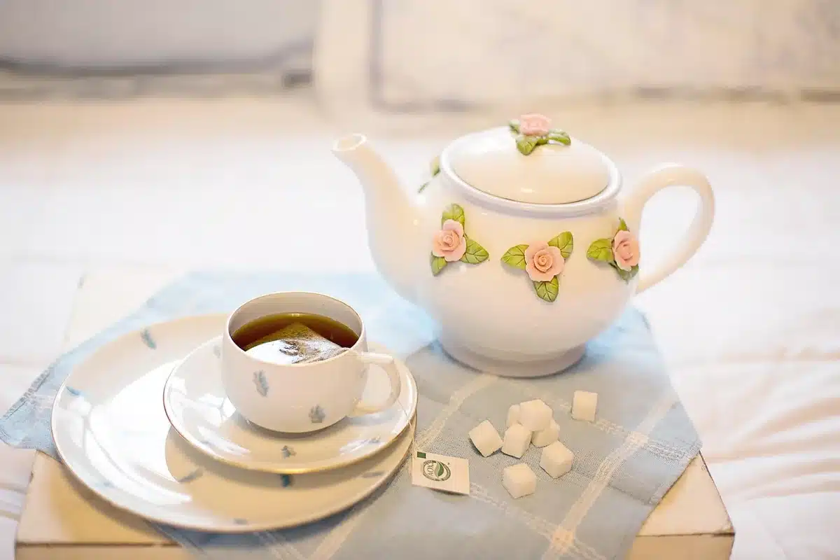 Manos sosteniendo un cuaderno junto a una taza de té frente a una ventana iluminada