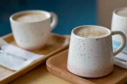 Manos anónimas hojeando un cuaderno junto a una taza y gafas en luz de mañana