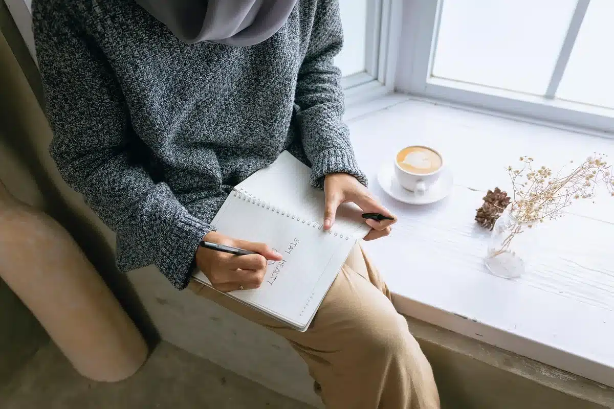 Manos anotando expectativas y gratitudes en un cuaderno, durante una práctica diaria de reflexión.