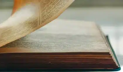 Manos anónimas sosteniendo un libro de filosofía abierto sobre una mesa junto a una taza y luz de ventana