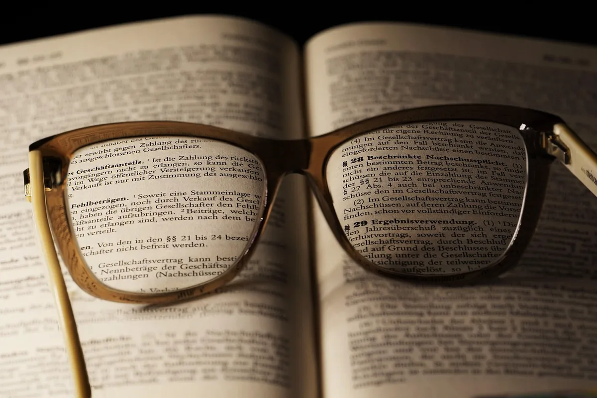 Manos sosteniendo un libro de filosofía con apuntes y una lámpara de lectura
